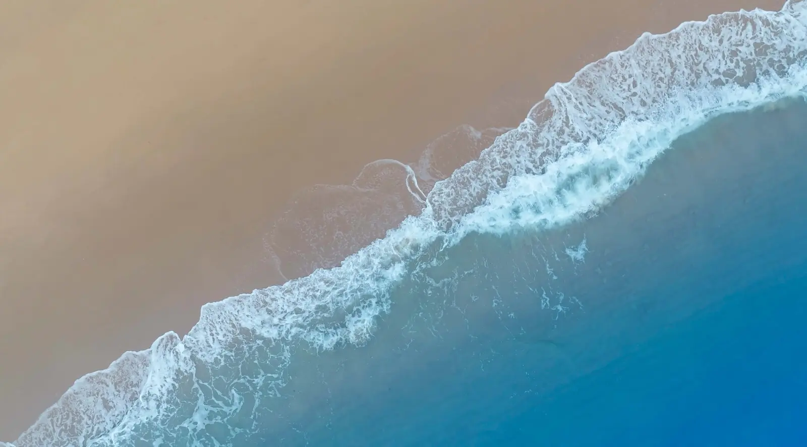 Aerial view of gentle sea waves rolling over pristine sand coast near Capeside Marina Residences Sobha Siniya Island.