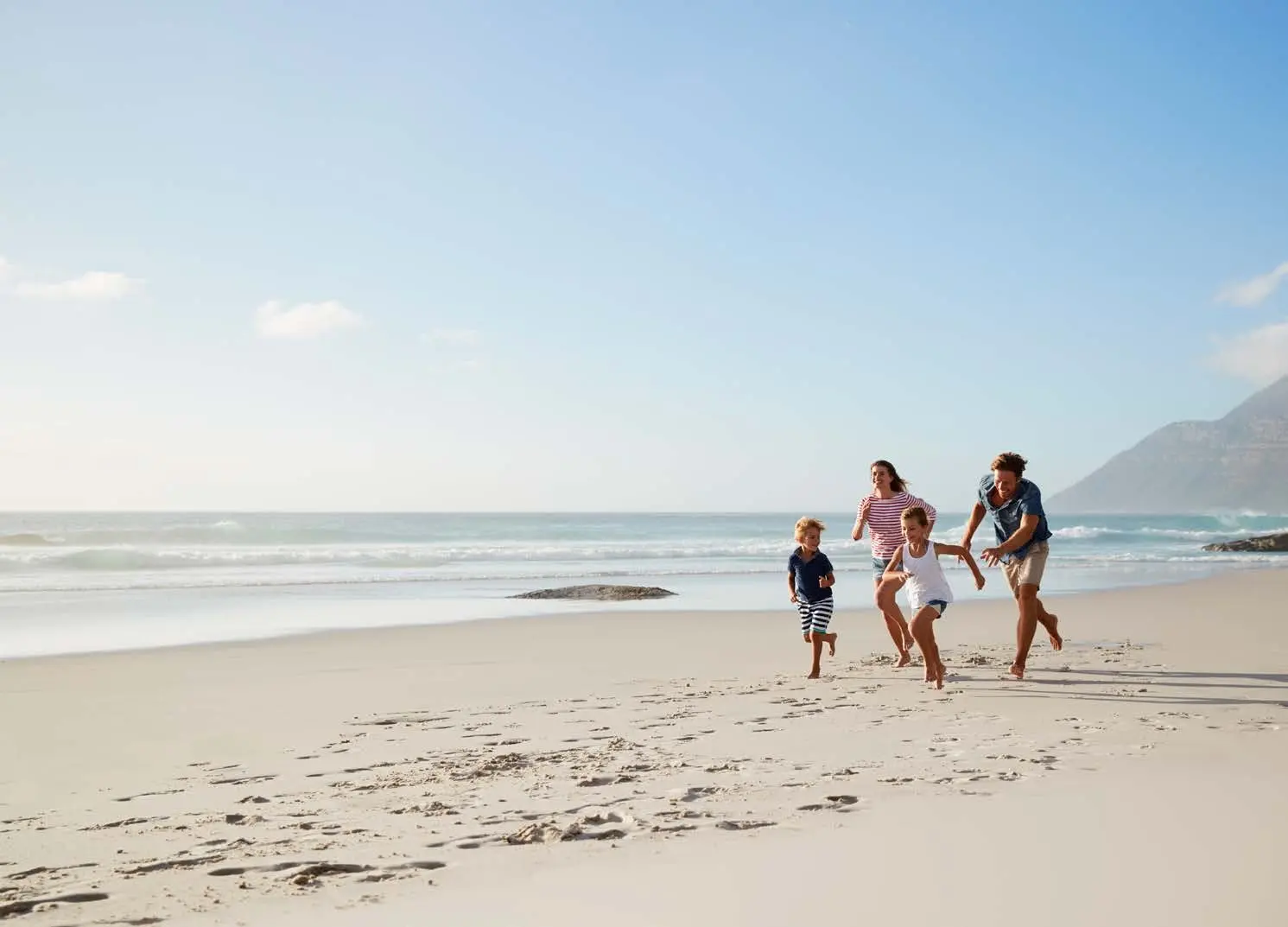 Happy family enjoying coastal lifestyle walks along white sand beach near Capeside Marina Residences Sobha Siniya Island.