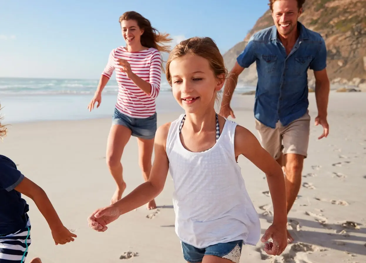 Joyful family running along the sunny white sand beach at Sobha Siniya Island near Bayfront Marina Residences.