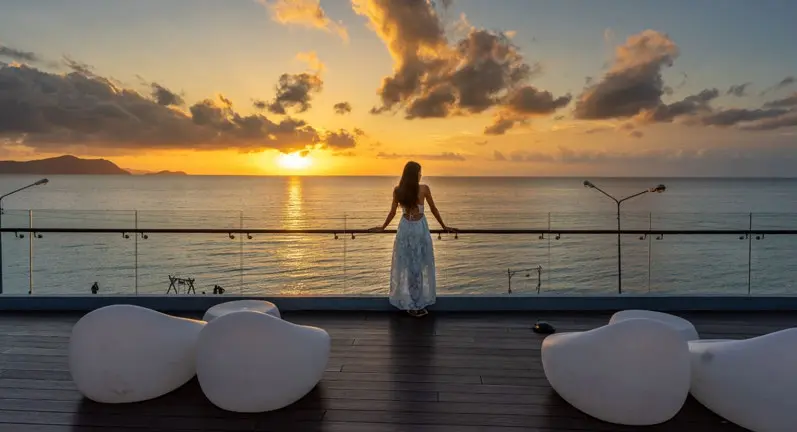 Woman standing on a rooftop terrace overlooking the sea during a golden sunset at Bayside Marina Residences on Sobha Siniya Island